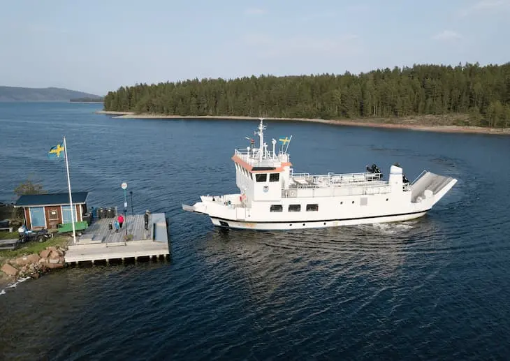 Färjan M/F Ulvön angör Västra Strängön. På bryggan finns anslagstavla, flaggstång, semafor och soptunnor. 